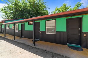 A row of green and black motel rooms with individual doors and windows.