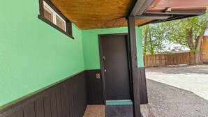 A covered porch with a green wall and a black door.