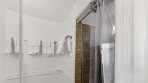 A bathroom with a toilet, a shower with a glass door, and multiple towels hanging on the wall.