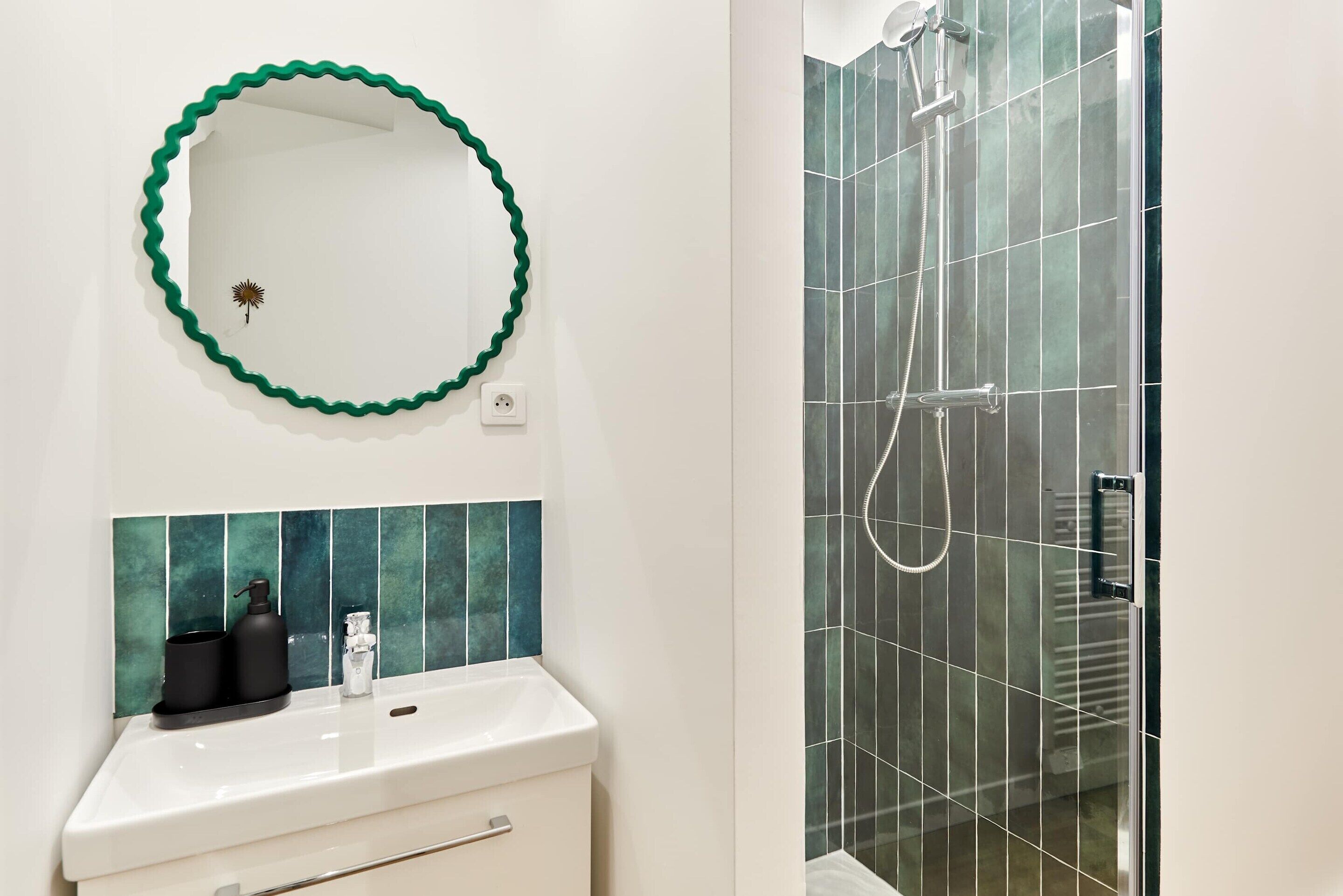 Un bagno con un lavandino bianco, uno specchio con cornice verde e una doccia rivestita di piastrelle verdi.