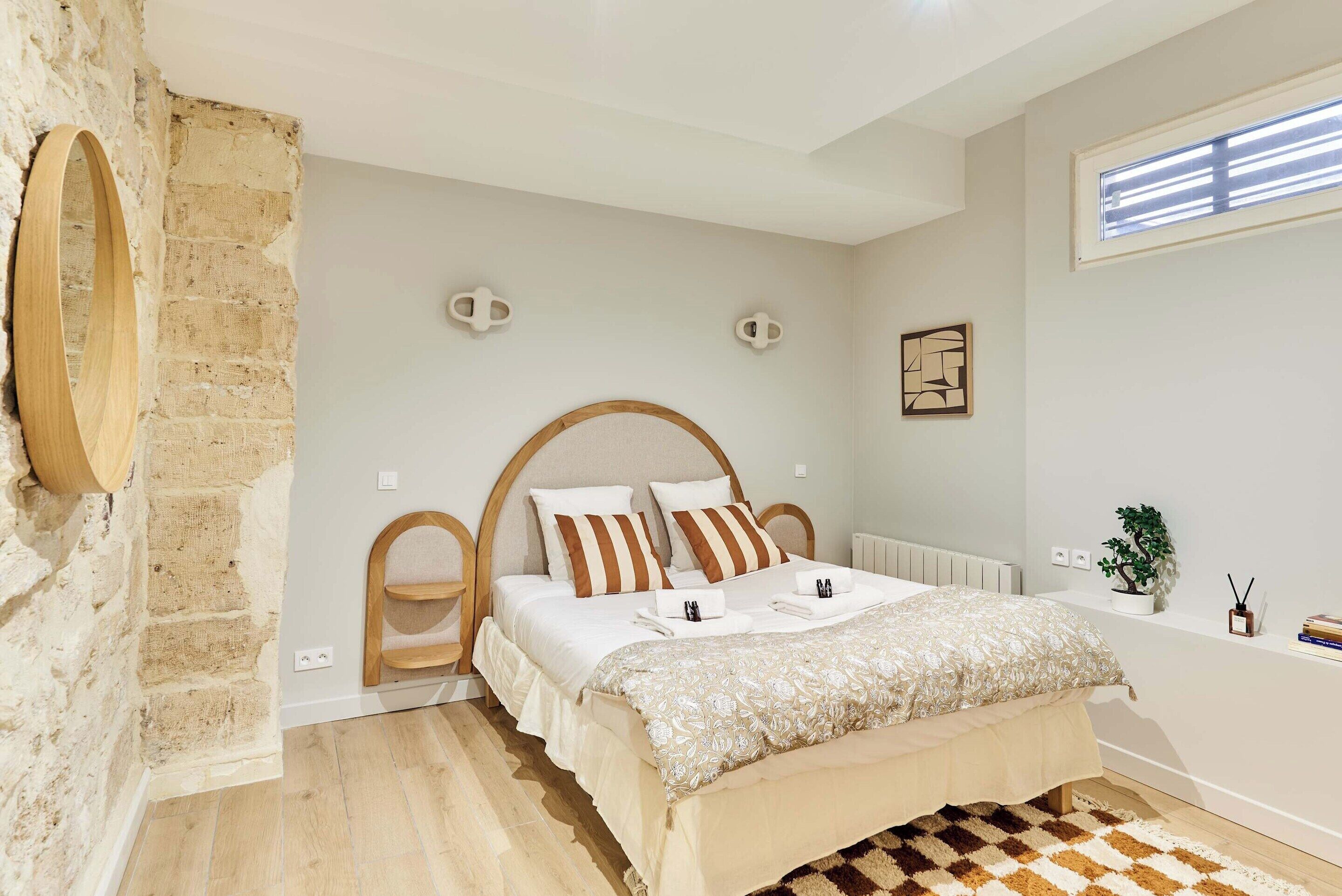 Una camera da letto con un letto, una testata in legno, un muro in mattoni, una finestra e una piccola pianta.