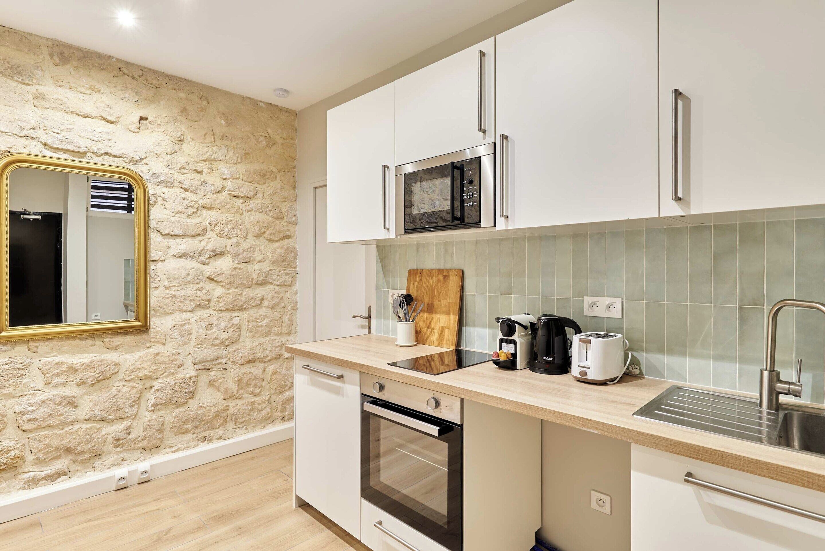 Eine moderne Küche mit weißen Schränken, einer Steinwand, einer Mikrowelle, einem Toaster und einem Spülbecken.