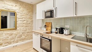 A modern kitchen with white cabinets, a stone wall, a microwave, a toaster, and a sink. - Charming Apartment Center of Paris by Studio Prestige (Paris)