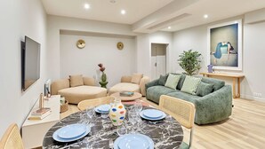 A modern living room with a dining table set for four, a green sofa, and a flat-screen TV mounted on the wall. - Charming Apartment Center of Paris by Studio Prestige (Paris)