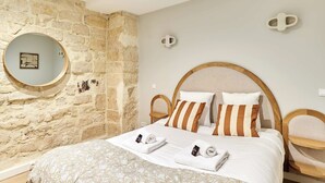 A hotel room with a stone wall, a round mirror, a bed with striped pillows, and a wooden headboard. - Charming Apartment Center of Paris by Studio Prestige (Paris)