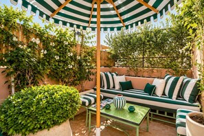 An outdoor seating area with a striped umbrella, a sofa with matching cushions, and potted plants. - Riad Casa Felicità (Marrakech)