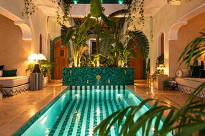 A pool area with a tiled floor, a seating area with a sofa and armchairs, and a wall with a mosaic pattern. - Riad Casa Felicità (Marrakech)