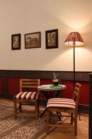 A room with two wooden chairs with striped cushions, a small round table with a green book and a candle, and three framed pictures on the wall.