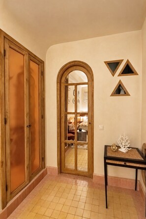 A room with a wooden door, a tiled floor, a small table with a decorative item, and a wall with geometric shapes. - Riad Casa Felicità (Marrakech)