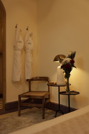 A wooden chair, two white robes hanging on hooks, a table with a candle and flowers, and a lamp. - Riad Casa Felicità (Marrakech)