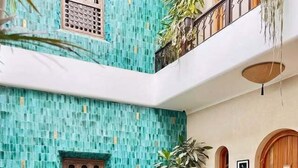 Ein mehrgeschossiges Interieur mit einer türkisfarbenen Mosaikwand, Holztüren und einem Balkon mit Metallgeländer.
