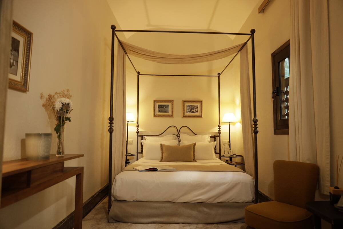 A four-poster bed with a canopy, bedside lamps, and a small table with a vase of flowers.