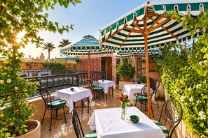 An outdoor patio with tables and chairs, surrounded by greenery and a view of the city. - Riad Casa Felicità (Marrakech)