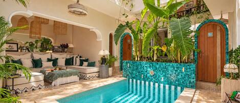 A pool area with a tiled floor, a sofa with cushions, and potted plants.