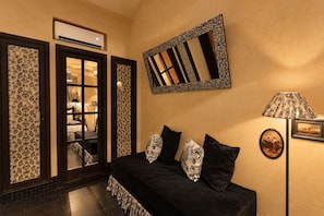 A room with a black sofa, patterned cushions, a mirror, a lamp, and a door leading to another room. - Riad Casa Felicità (Marrakech)