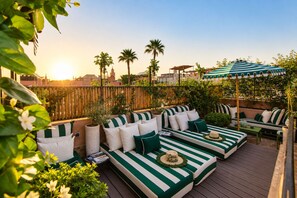 A rooftop deck with green-striped outdoor furniture, a wooden fence, and a view of the city skyline. - Riad Casa Felicità (Marrakech)