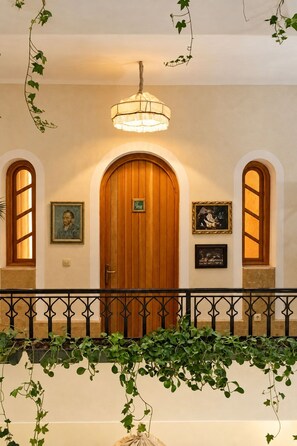 A hallway with a wooden door, two framed pictures, a hanging light fixture, and a black wrought iron railing. - Riad Casa Felicità (Marrakech)