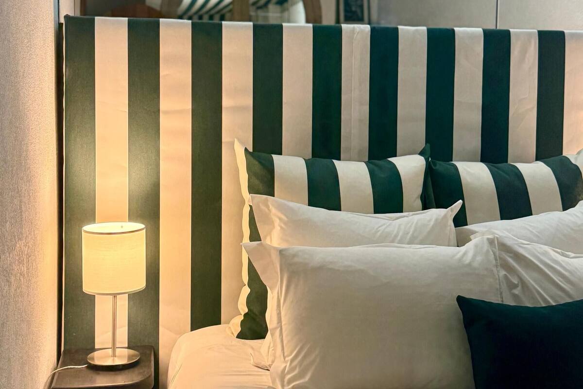 A bed with striped headboard, white and dark green pillows, and a bedside lamp.