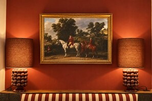 A framed painting of horsemen on horseback, flanked by two wall-mounted lamps with textured shades. - Riad Casa Felicità (Marrakech)