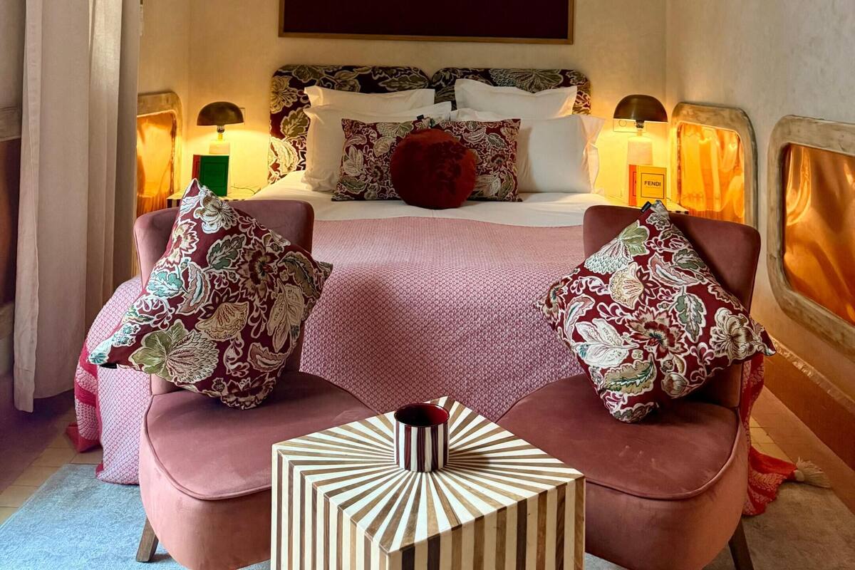 A hotel room with a bed, two bedside lamps, a large mirror, and a small side table with a decorative item.