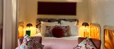A hotel room with a bed, two bedside lamps, a large mirror, and a small side table with a decorative item.