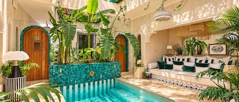 A luxurious indoor pool area with a tiled floor, surrounded by lush greenery and a comfortable seating area with cushions.