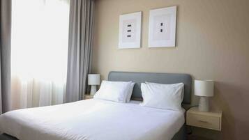 A hotel room with a bed, two bedside lamps, a nightstand, and a window with curtains.