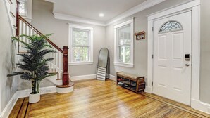 A hallway with hardwood flooring, a staircase with a wooden handrail, a potted plant, a bench, and a white door with a decorative glass window. - Hilltop Retreat w/ Pool, Games & Sunroom (Woodlawn)