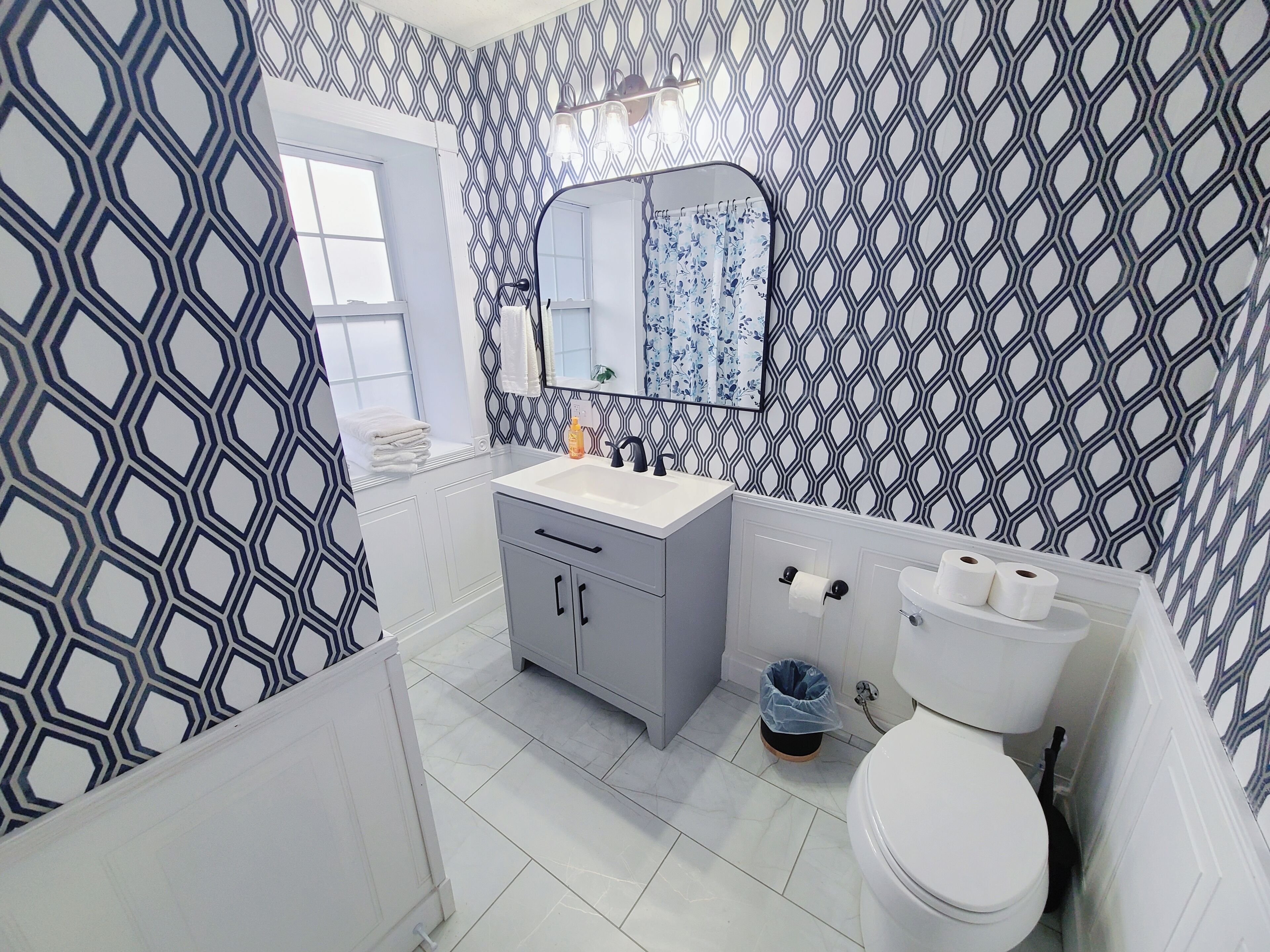 Une salle de bain avec un mur à motifs, un lavabo, un miroir, des toilettes et une poubelle.