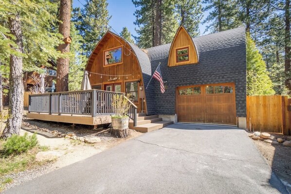 A cabin with a wooden deck, a garage, and a large window.