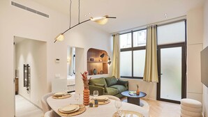 Ein modernes Wohnzimmer mit Essbereich, einer Couch, einem Couchtisch und einem großen Fenster mit Vorhängen.