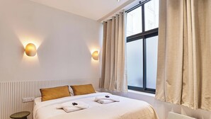 Ein modernes Hotelzimmer mit Bett, Nachttischlampen, einem Fenster mit Vorhängen und einer Heizung.