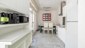 A modern kitchen with white cabinetry, a marble floor, and a dining area with white chairs. - Modern Apartment - 2br-4p- Croisette Plage (Cannes)