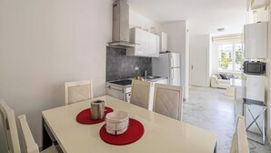A modern kitchen with white cabinets, a grey backsplash, and a dining area with a white table and chairs. - Modern Apartment - 2br-4p- Croisette Plage (Cannes)
