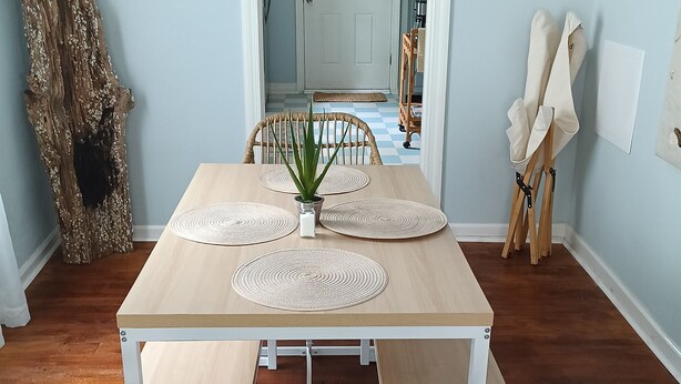 Un comedor con una mesa de madera, sillas tejidas y un espejo grande que refleja la habitación.