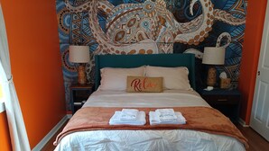 Un lit bien fait, avec une tête de lit de couleur turquoise, un coussin orné du mot «Relax», et une table de chevet en bois sur laquelle se trouvent une lampe et un panier.
