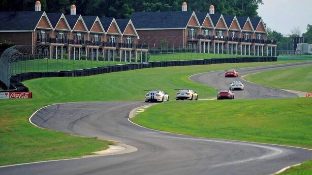 A race track with multiple cars, a Coca-Cola advertisement, and a row of houses in the background.