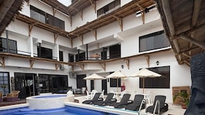 Ein Innenpool mit Liegestühlen und Sonnenschirmen, umgeben von einem mehrstöckigen Gebäude mit einem Strohdach.