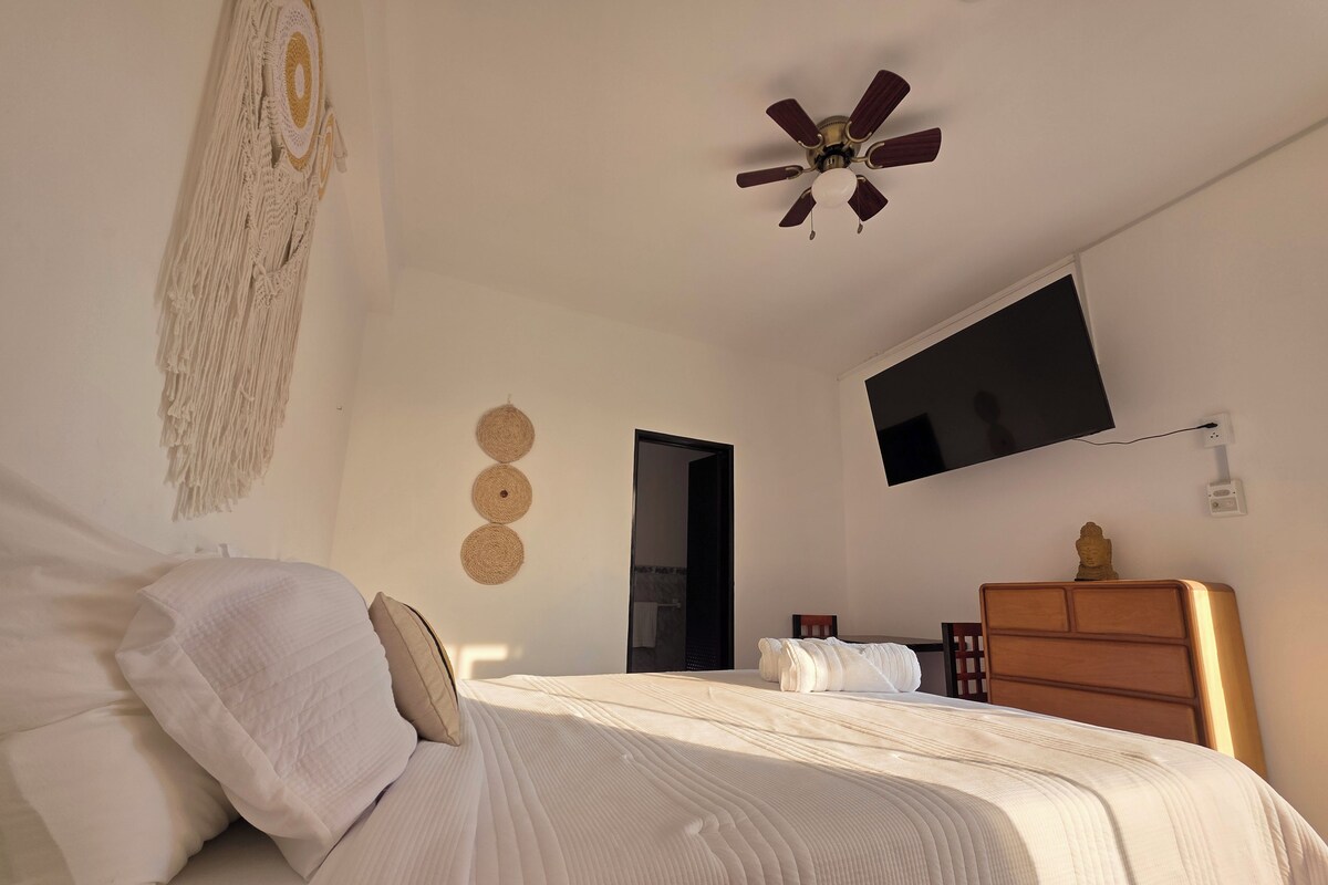 A bedroom with a bed, a ceiling fan, a TV, and a wooden dresser.
