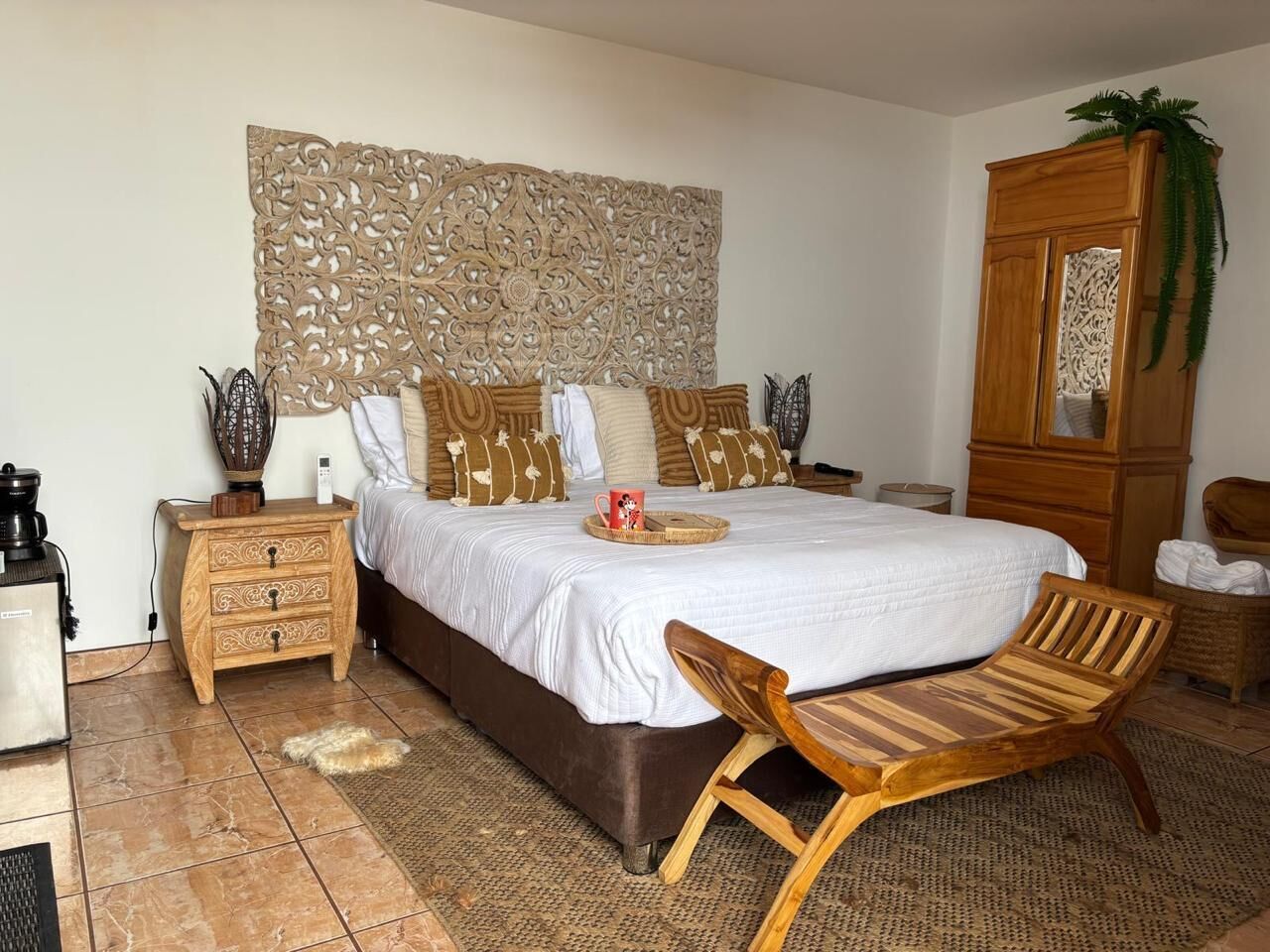 A bedroom with a large bed, wooden headboard, a wooden nightstand, a wooden chair, and a wardrobe.