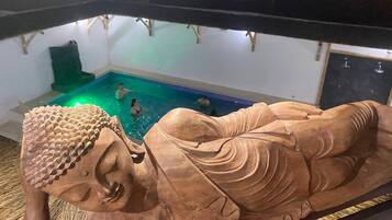 Una gran estatua de Buda de madera en una habitación con piscina.