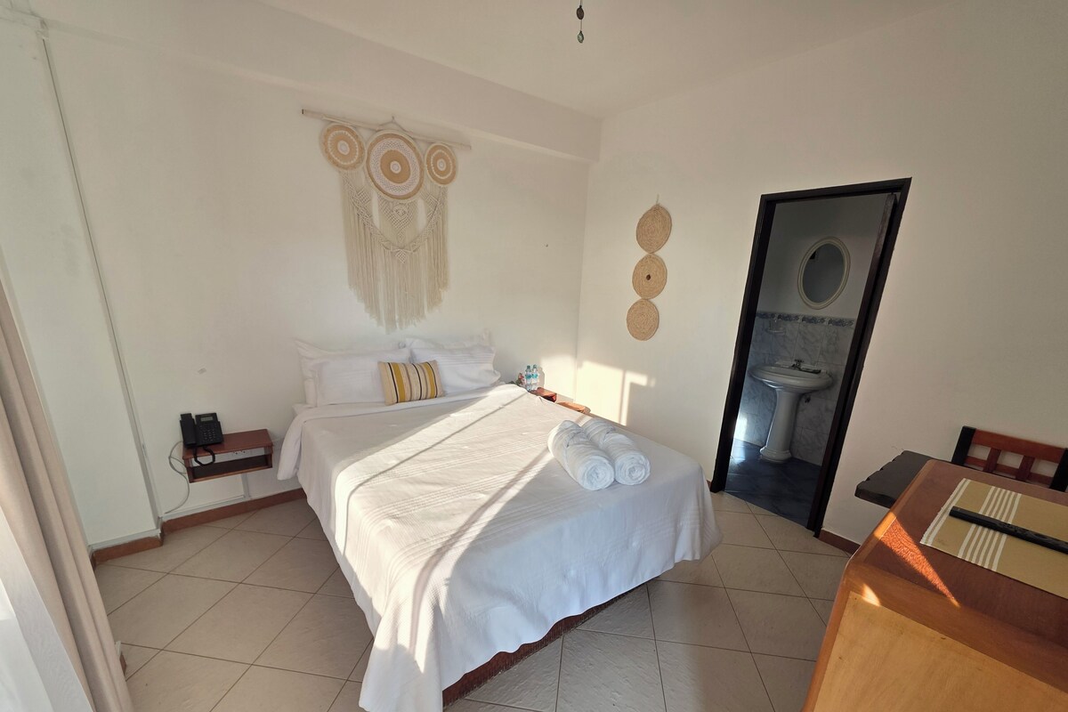 A hotel room with a bed, a bedside telephone, a mirror, and a bathroom visible through an open door.