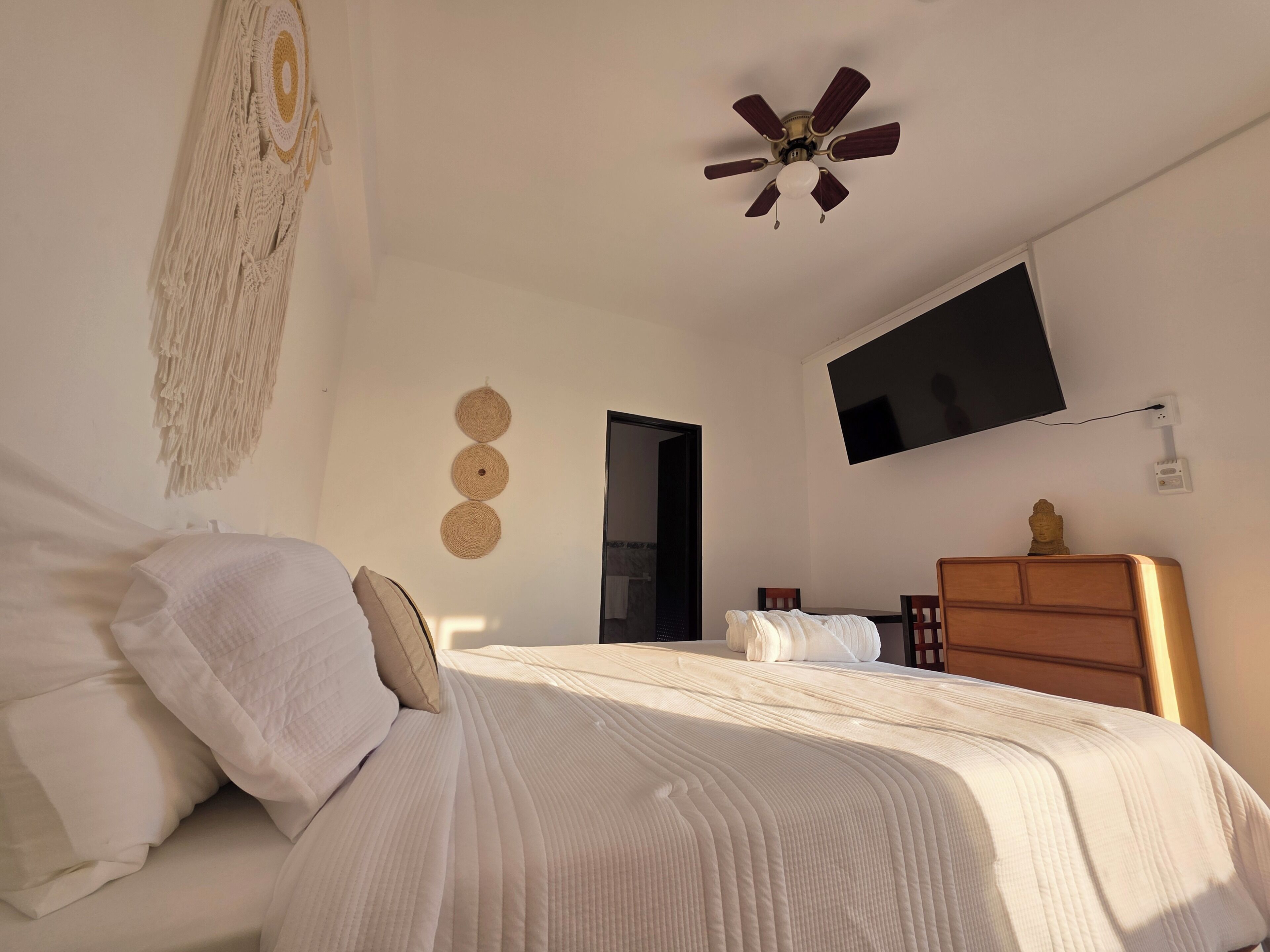 A bedroom with a bed, a ceiling fan, a TV, and a wooden dresser.