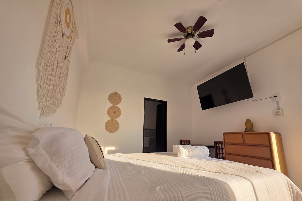 A bedroom with a bed, a ceiling fan, a TV, and a wooden dresser.