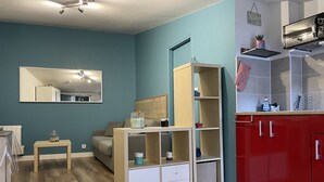 Een knus woongedeelte met een kitchenette, een spiegelwand en een klein tafeltje met spullen erop.