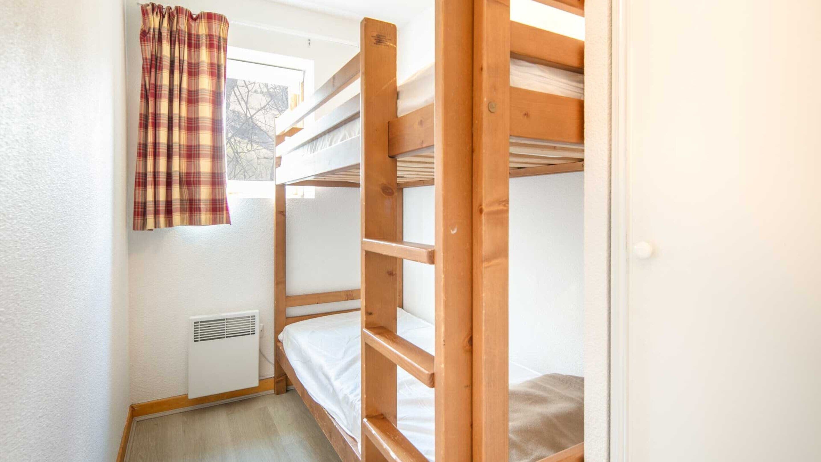 Ein Schlafzimmer mit Etagenbetten, einem Fenster, einer Heizung und einem Karomuster-Vorhang.