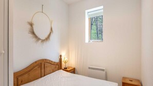 Un dormitorio con una cama de madera, una lámpara de noche, una ventana con vistas a árboles y una corona colgando en la pared.