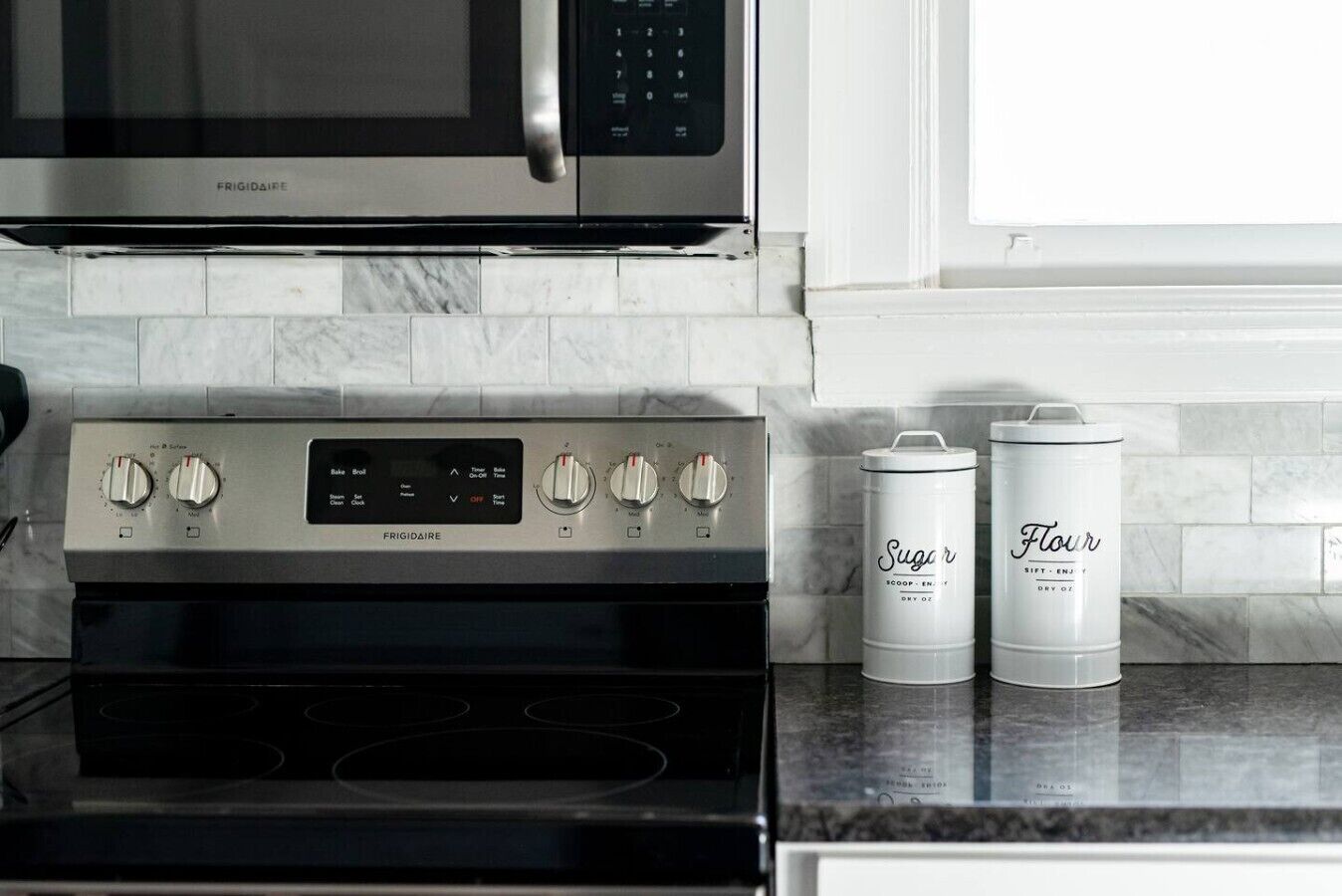 A kitchen with a Frigidaire oven, a microwave, and two white containers labeled 'Sugar' and 'Flour'.