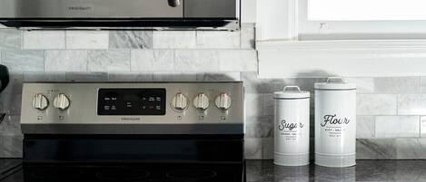 A kitchen with a Frigidaire oven, a microwave, and two white containers labeled 'Sugar' and 'Flour'.