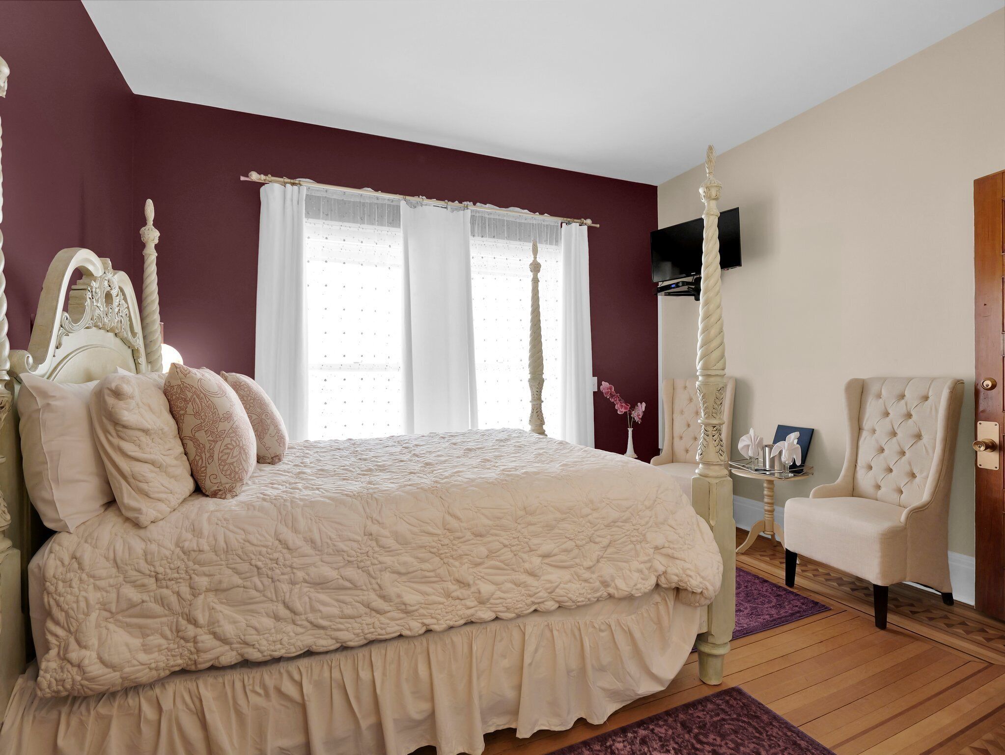 A bedroom with a four-poster bed, a chair, and a television on the wall.
